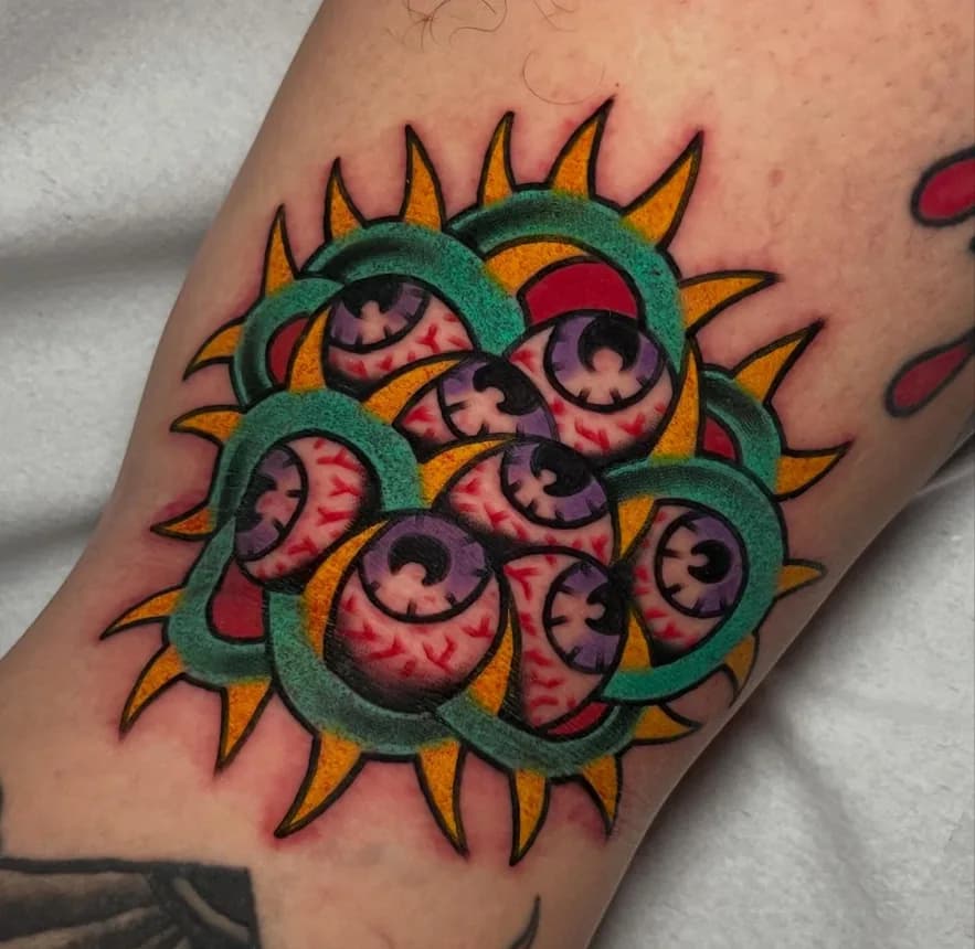 Traditional tattoo of a cluster of eyeballs framed by a green spiked sunburst, on the forearm