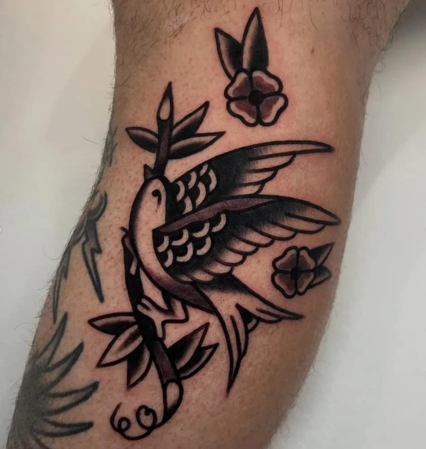 Black and grey traditional swallow tattoo with flowers, on the forearm