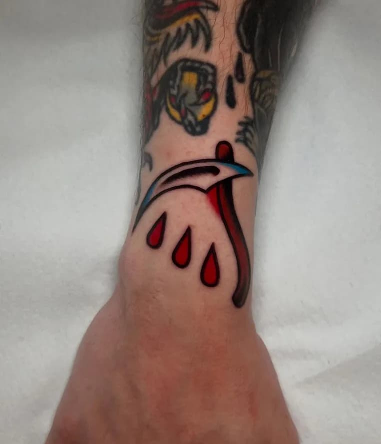 Traditional colorful bloody scythe tattoo, on the wrist