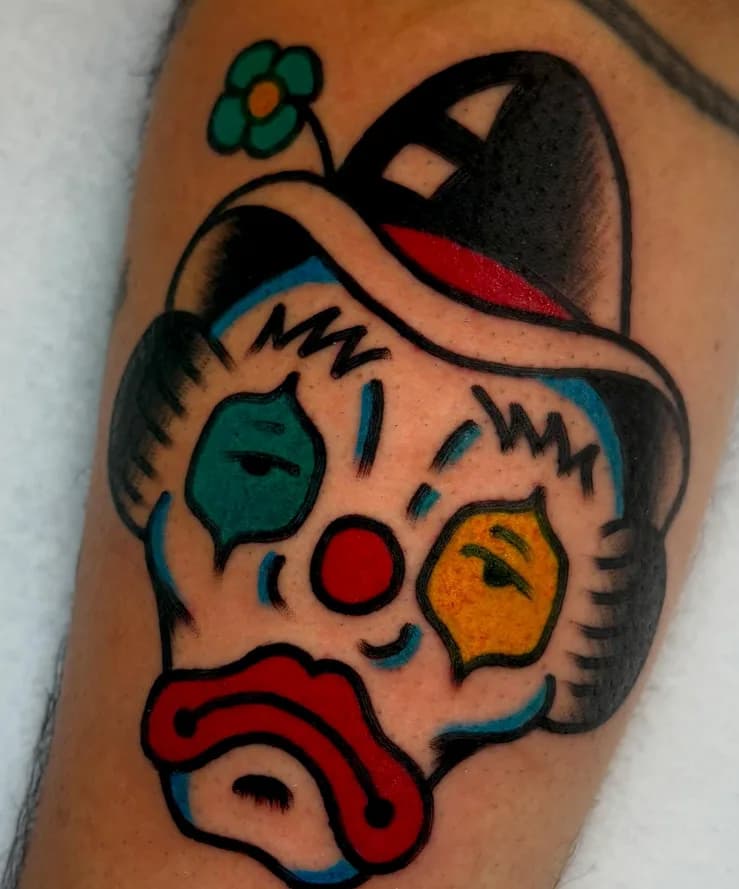 Traditional colorful sad clown tattoo with a top hat, on the arm